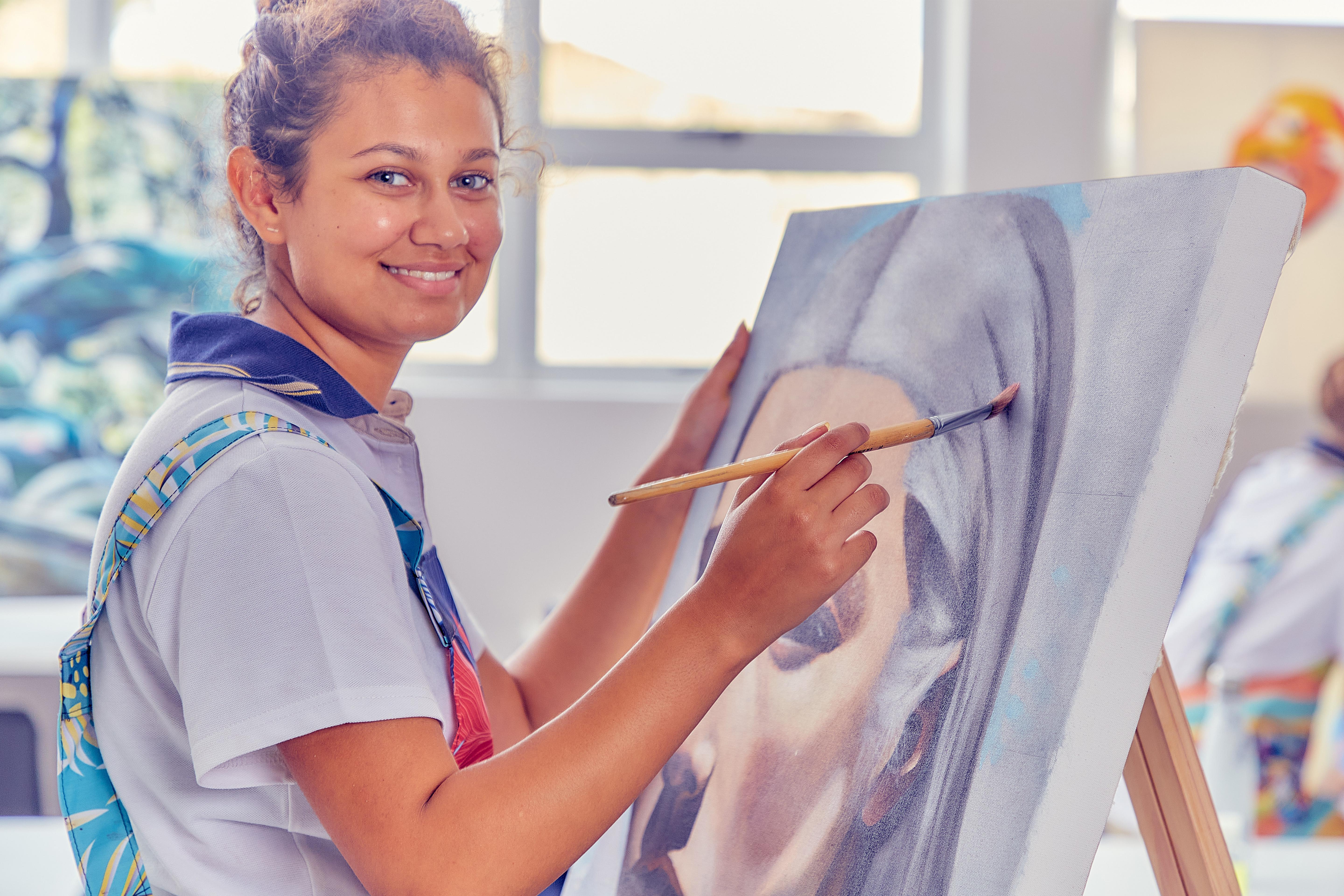 Student looking at the camera with a paintbrush in hand