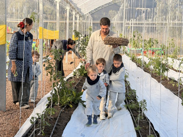 an-adult-guides-a-small-group-of-young-children-along-a-planting-row-inside-a-greenhouse