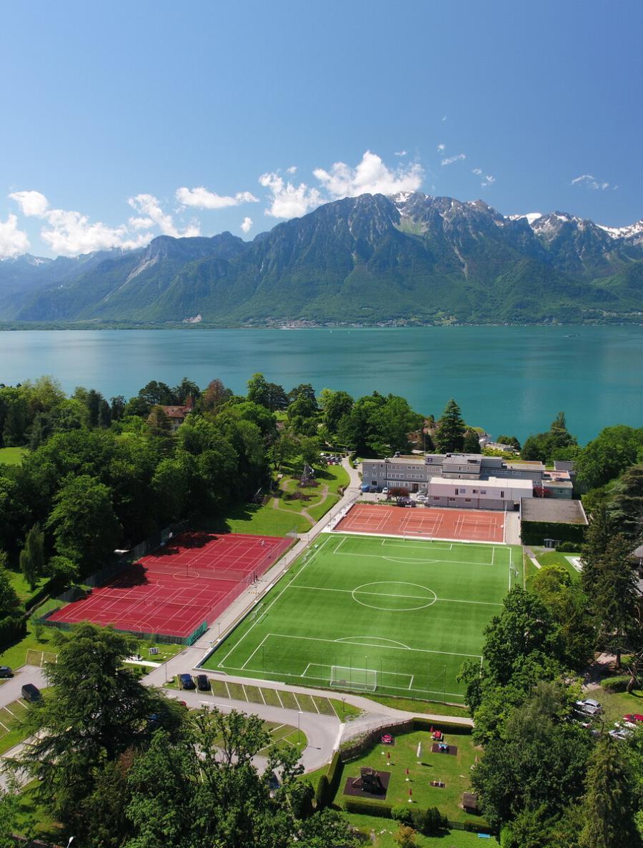Aerial view of a lakeside boarding campus in the Alps with a football pitch