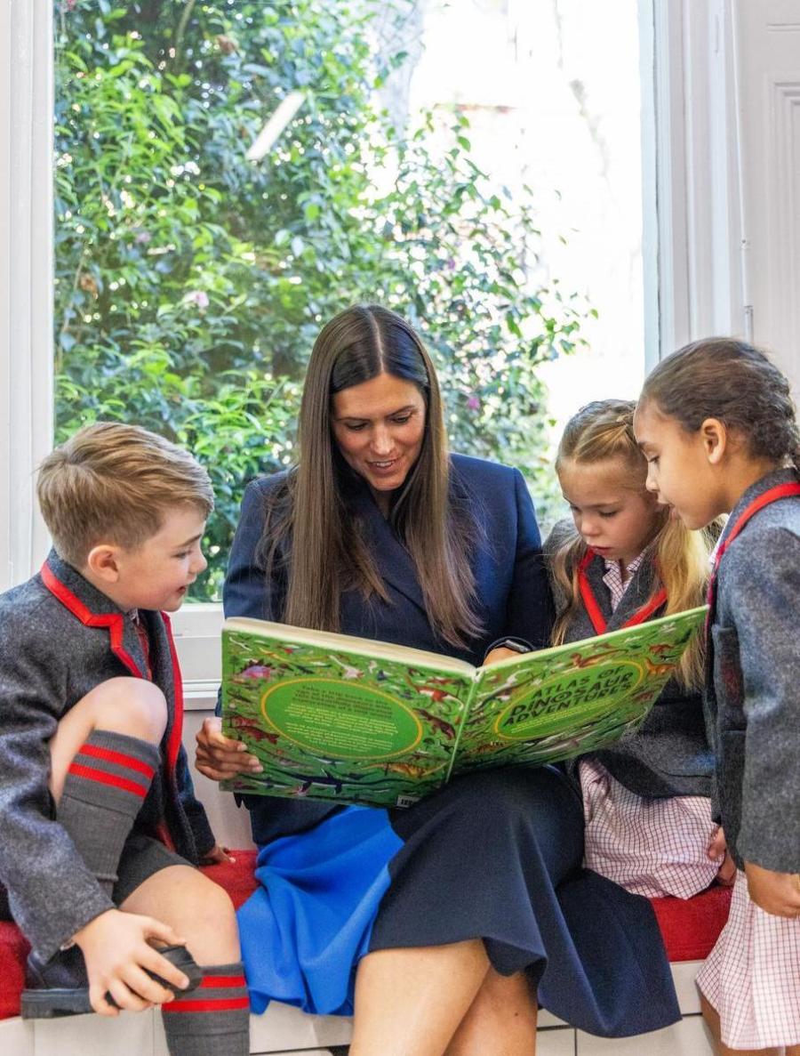 Adult with two students reading a book together