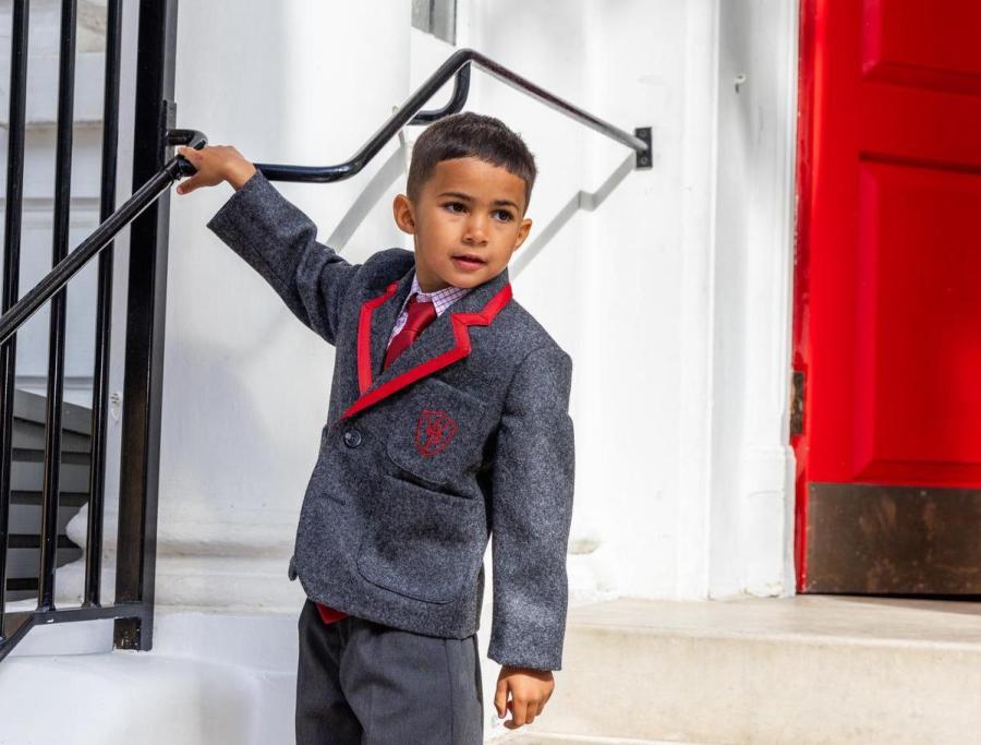 Boy in a grey blazer with red trim holding a stair railing beside a red door