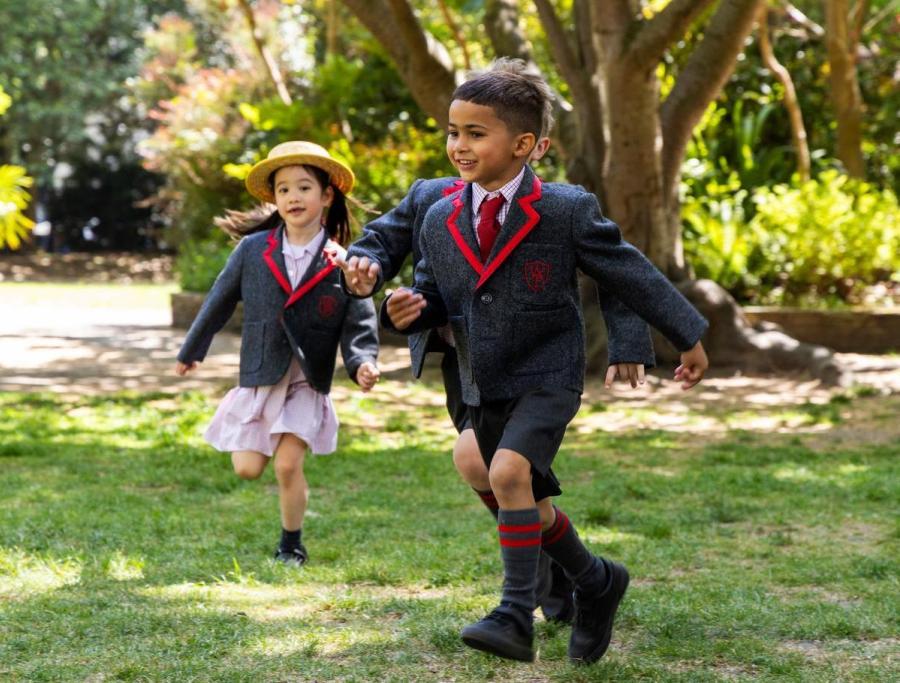 Two pupils in school uniform running across a sunny lawn