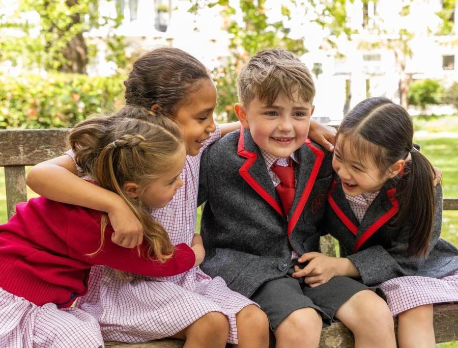 Four pupils hugging and laughing together on a garden bench