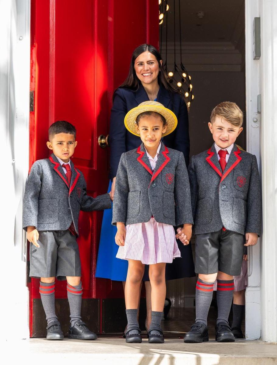 Teacher and three pupils in uniform at the school's red front door