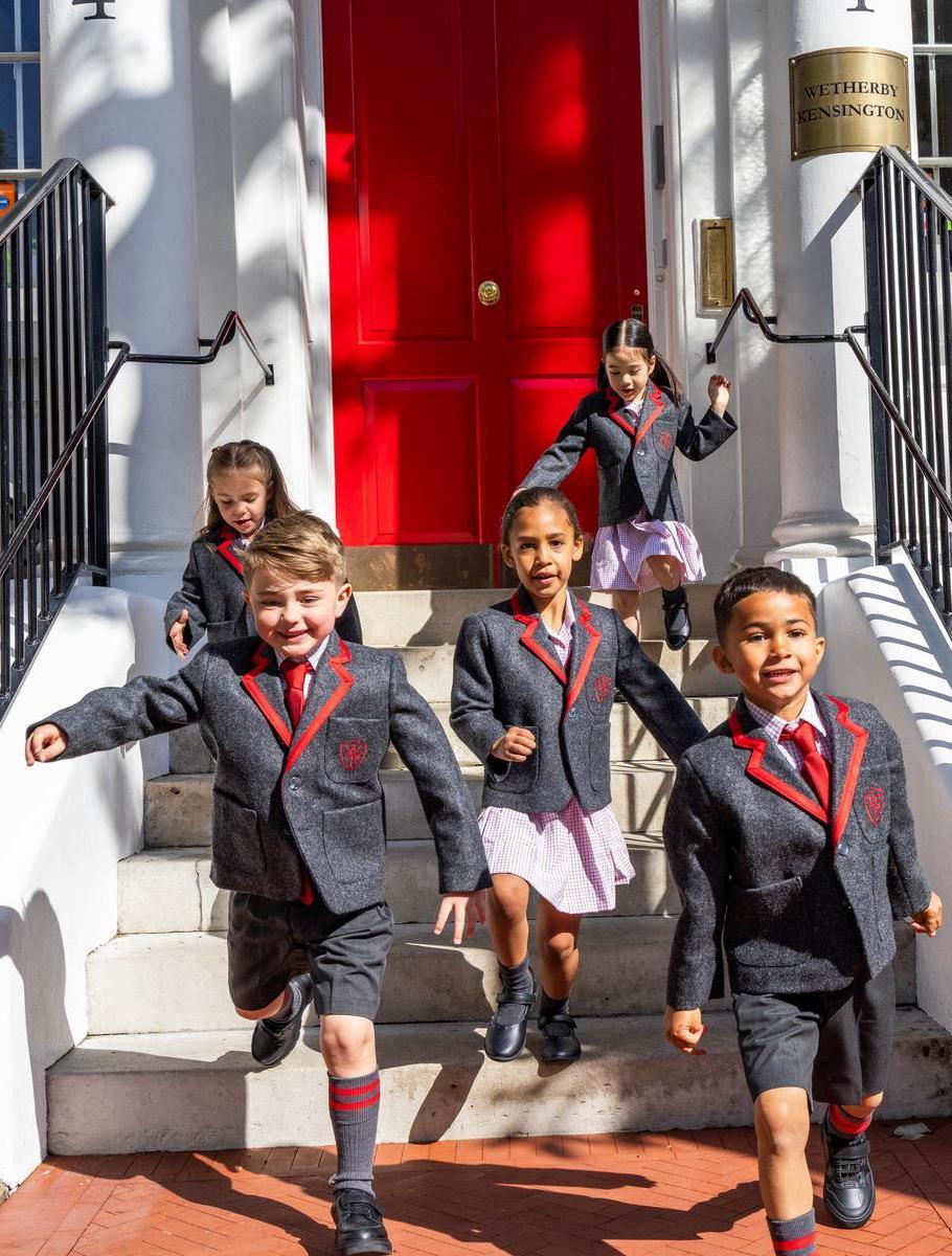 Pupils in uniform coming down white steps in front of the red school door